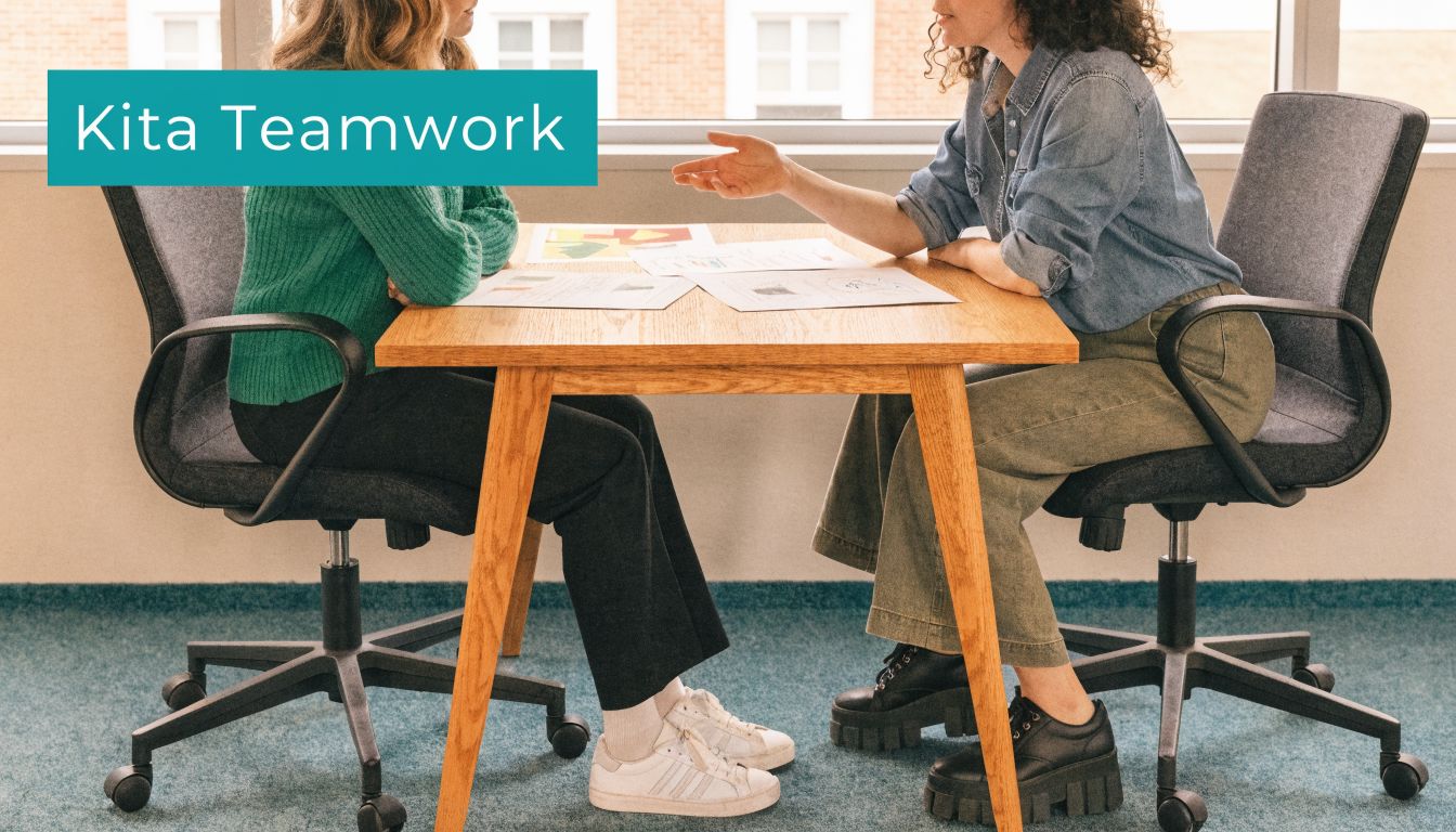 Zwei Erzieherinnen sitzen an einem Holztisch und besprechen gemeinsam Unterlagen im Rahmen ihrer professionellen Zusammenarbeit in der Kita.