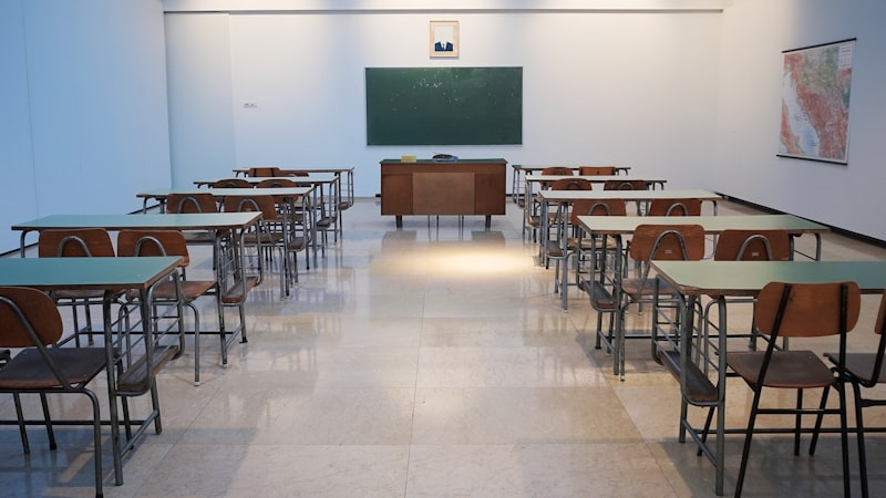 Eine Schulsozialarbeiterin spricht einzeln mit einem Schüler in einem hellen Klassenraum während andere Kinder im Hintergrund arbeiten.